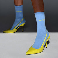 Yellow high-heeled shoes with blue socks worn by a person on a gray background